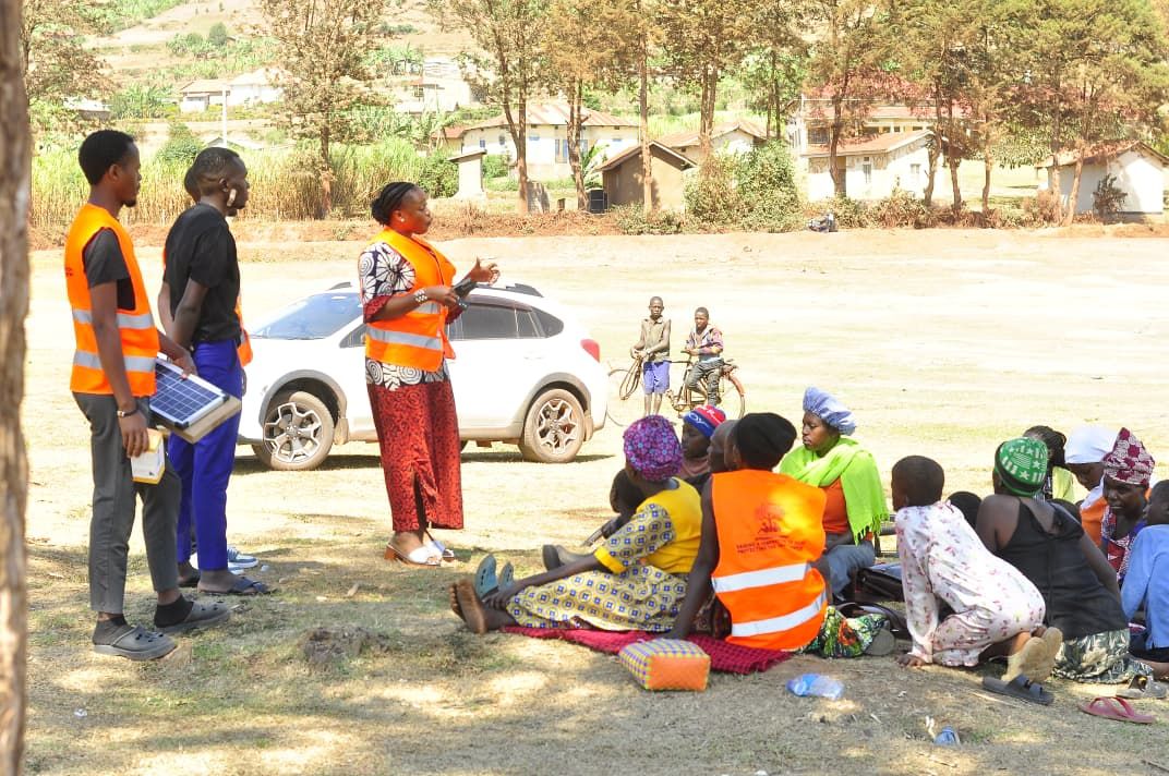 Volunteer addressing families seated on the ground, holding a solar panel